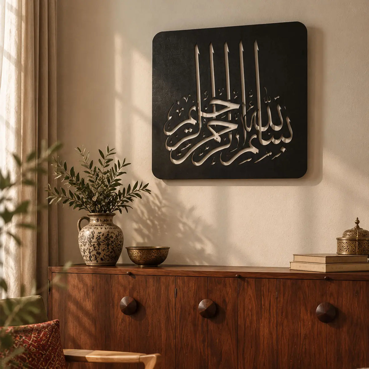 Bismillahirrahmanirrahim yazılı siyah metal Kufi hat tablosunun aydınlık bir yaşam alanında kullanımı; modern İslami ev dekorasyonu, manevi duvar sanatı ve yeni ev hediyesi arayanlar için dekoratif Besmele tasarımı.
